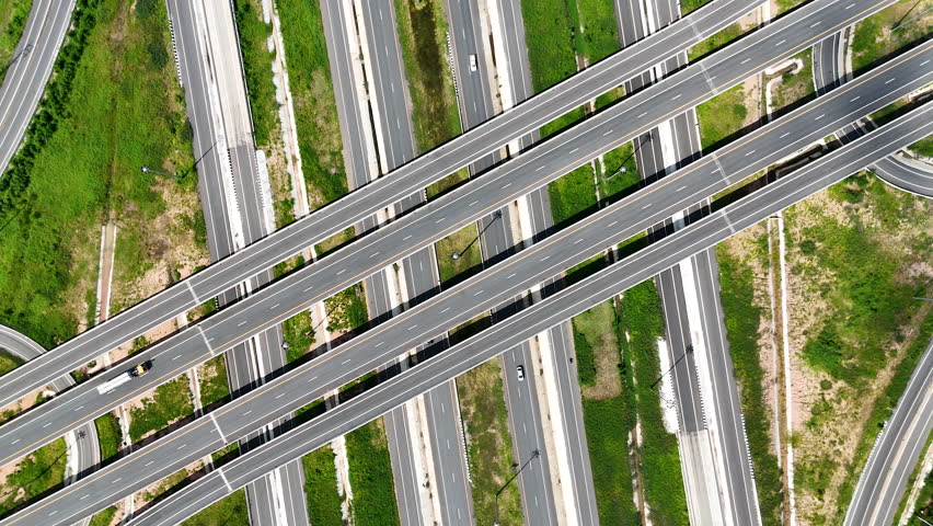 Aerial view of modern highway interchange with multilayer roads and curved ramps surrounded by green farmland, showcasing transportation infrastructure, urban development, and road network planning.