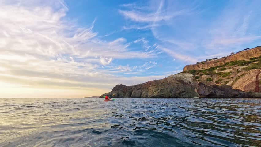 Kayaking sea sunset man rowing orange boat near rocky cliffs for summer adventure and outdoor fitness