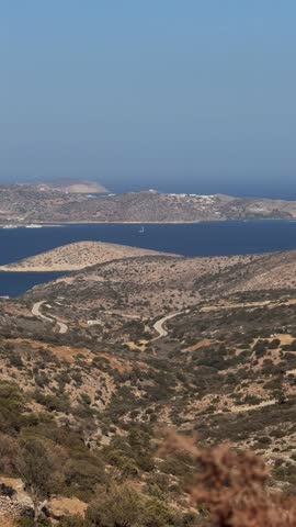 Mountain slope overlooking dry Cycladic island landscape, small island with white houses and boat on Aegean Sea
