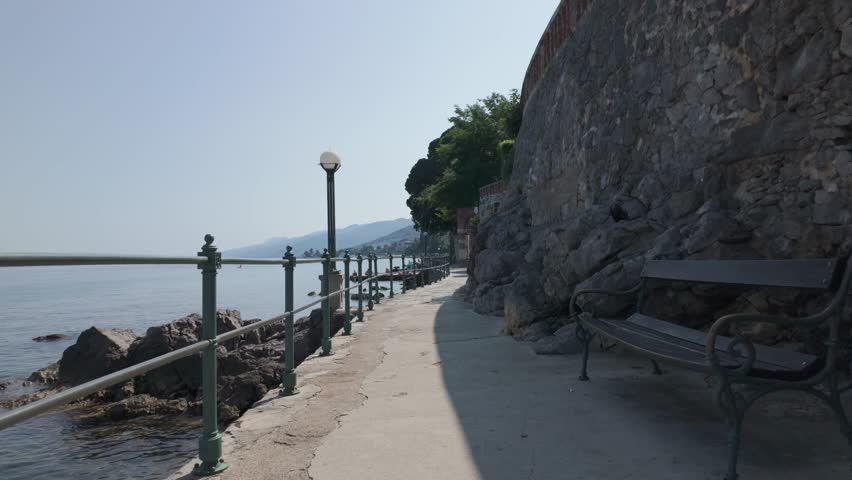 
Walking along the Lungomare Coastal Promenade in Volosko, Croatia on a sunny summer day. Rocky Adriatic Sea coastline with railings and blue water. The famous seaside walkway is over 100 years old.