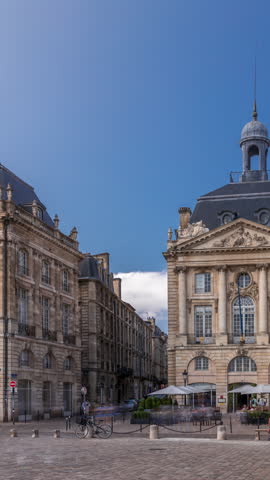 Place de la Bourse timelapse hyperlapse in Bordeaux, France, with restaurants surrounded by classic architecture under a cloudy blue sky. People walking around the main square and central streets
