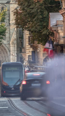 Timelapse of Bordeaux Cathedral entrance (Cathedrale Saint Andre) from Vital Carles street, featuring a moving tram in the historic city. People wait at the tram stop. A symbol of heritage. France