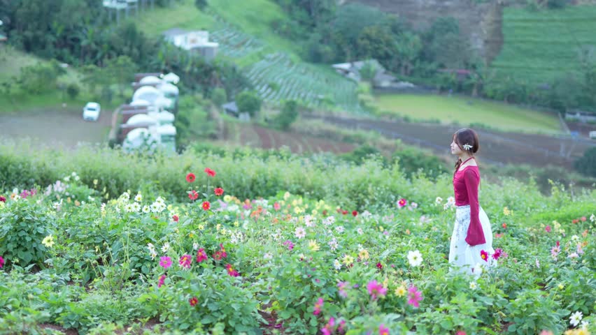  A young woman stands amidst a field of flowers at sunset.
