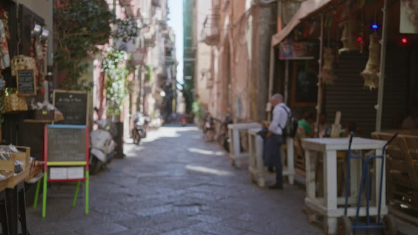 Narrow alley with defocused bokeh background showing market stalls, scooters and textured paving in a soft blur; background backplate copyspace.