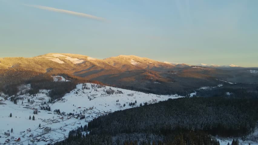 panoramic view of a serene rural village nestled in a snow-covered valley, with the last golden light of sunrise or sunset illuminating the snowy peaks of the Carpathian Mountains in Ukraine.