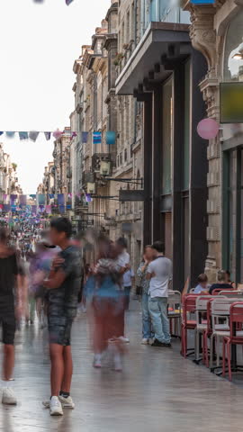 Tourists and locals walking and shopping in Rue Sainte-Catherine timelapse, Bordeaux, France. The longest pedestrian street in the country. Colorful flags decorate the street. Atmosphere of urban life