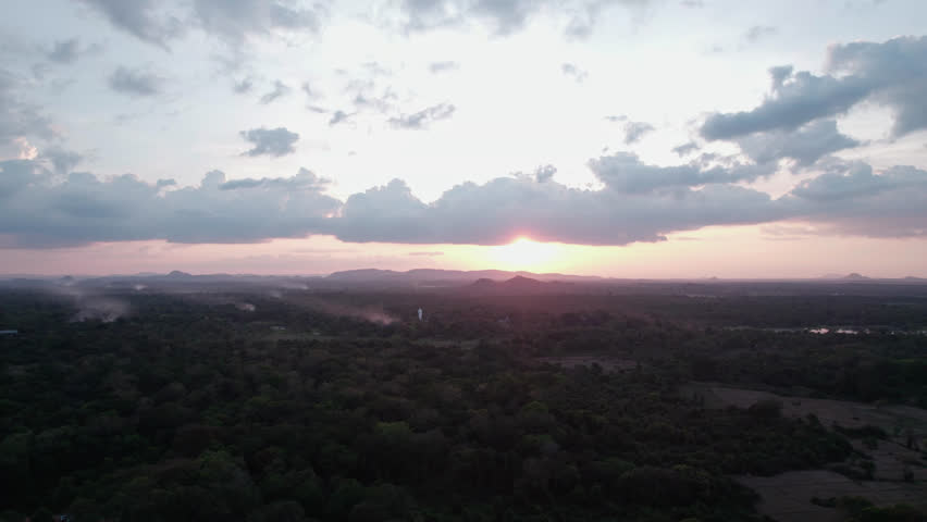 Drone view of sunrise above a vast tropical forest and distant hills in Sri Lanka, with dramatic clouds and soft morning light creating a calm natural panorama.