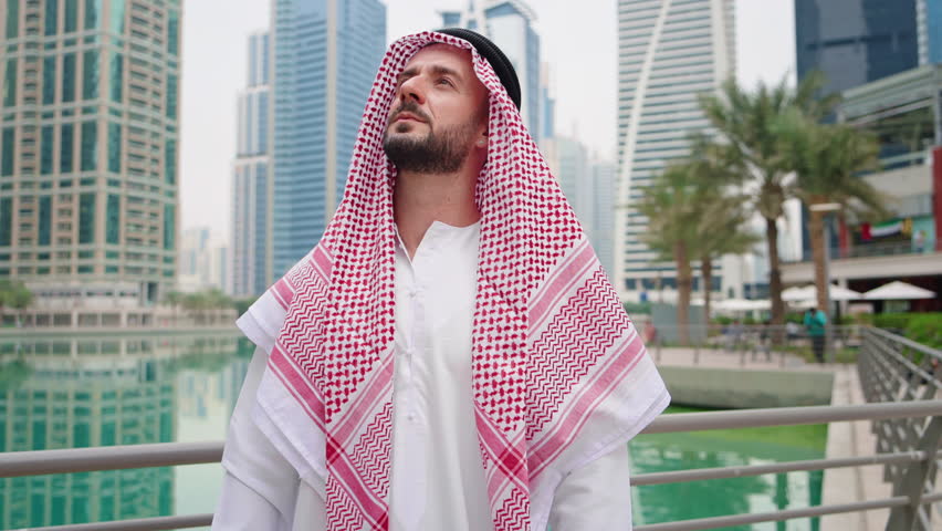 An Arab businessman stands alone in a modern urban area, displaying confidence and hope for future success in real estate business.