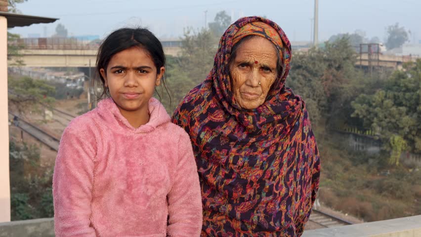 Elderly indian woman and young Indian  girl standing together outdoors, smiling and posing for the camera. Concept of family, bonding, generations, and everyday life in India.