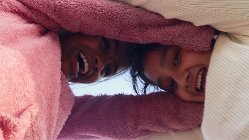 Two young Indian girls laughing and playing together outdoors, captured from a low angle, showing joy, friendship, and carefree childhood.