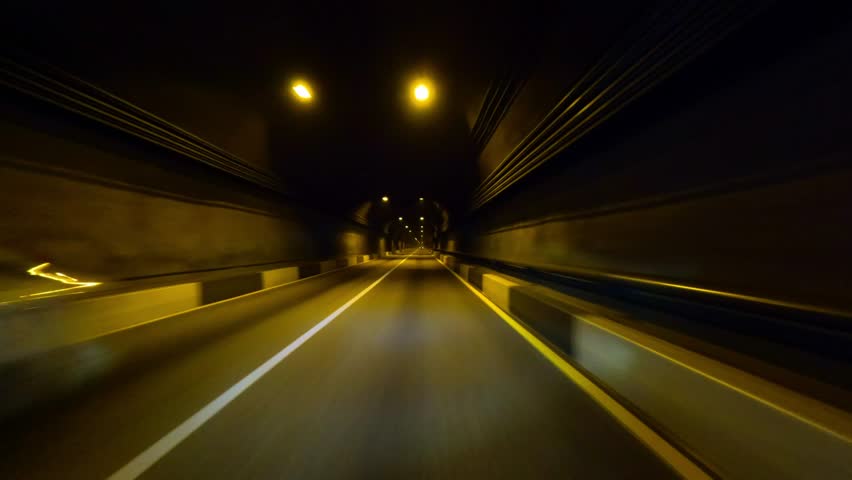 A first-person view from inside a car driving through an underground tunnel in the mountains. Low lighting and high speed. Shot with an action camera.