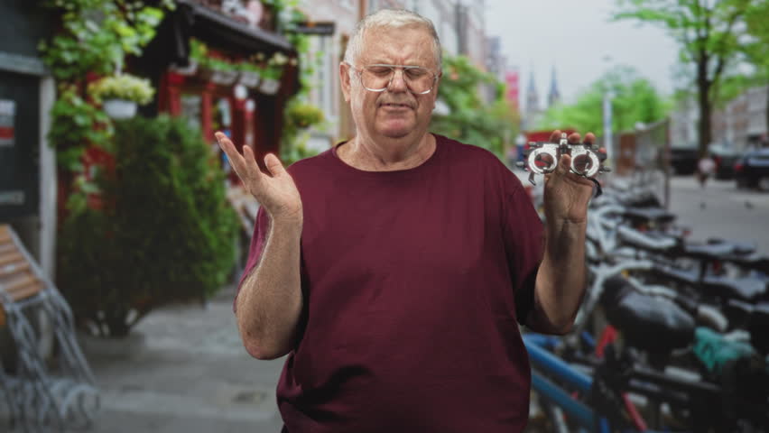 Elderly man holding a trial frame and raising one hand on a street with bicycles and storefronts; vision concern.