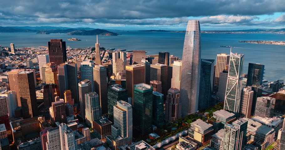 Moving over the tops of high-rises approaching the highest skyscraper. Salesforce Tower in the downtown of San Francisco, CA, USA. Dramatic cloudscape over the waterscape ta backdrop.