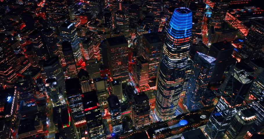 Flying above the blue neon top of Salesforce Tower in the downtown San Francisco. View of the vibrant lively city from drone at night.