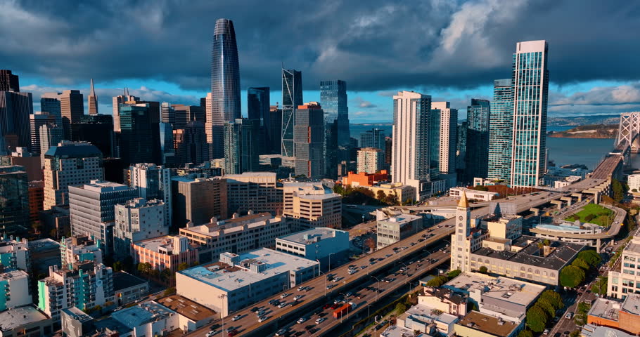 Flying over busy highways crossing the downtown. Skyline of San Francisco, CA, USA against cloudy sky.