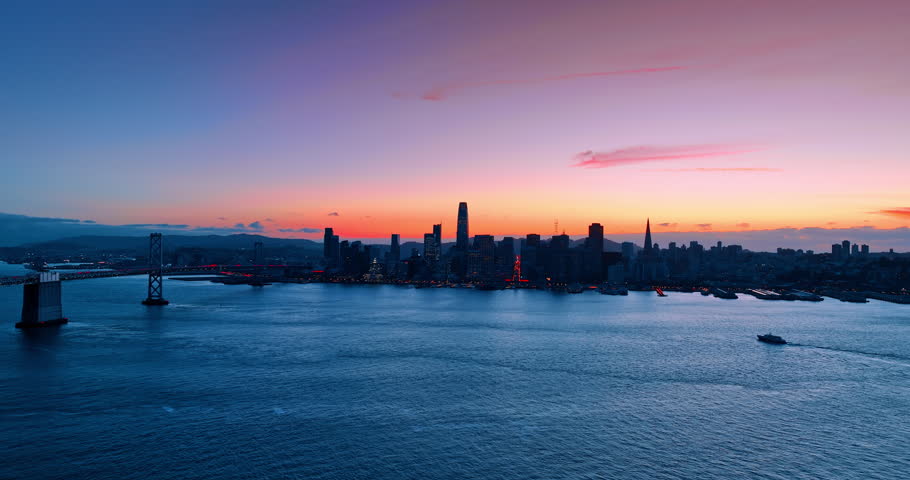 Skyline silhouette of San Francisco, California, USA. Lots of cars with headlights on move by the San Francisco-Oakland Bay Bridge at dusk time.