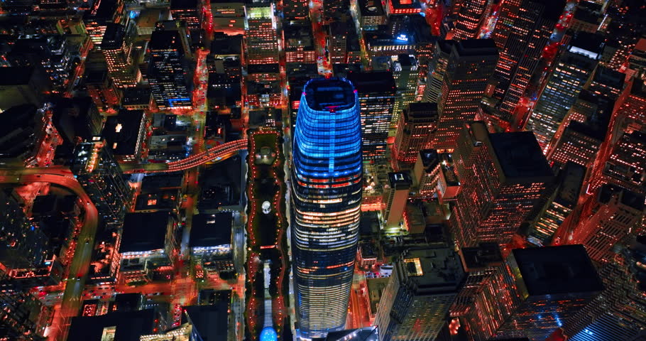 Flying over the top of Salesforce Tower lit with blue neon light. Dazzling panorama of downtown San Francisco, California, USA at night.