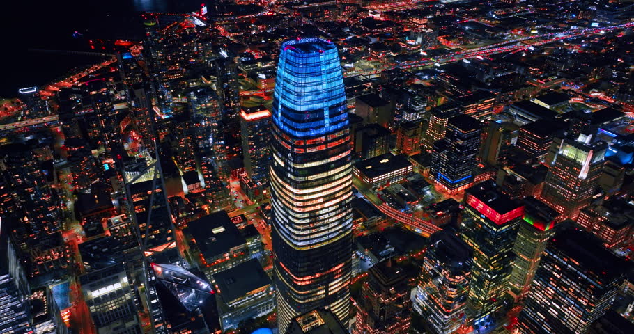 Footage over high-rise downtown of San Francisco, California, USA at night. Drone flight near Salesforce Tower with neon lit top.