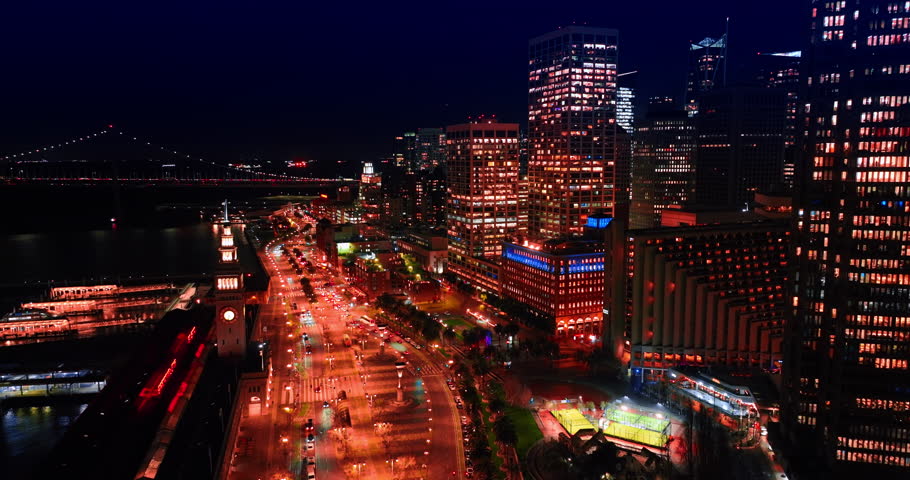 Brightly illuminated waterfront of San Francisco, California, USA. Revealing view on the dark bay and bridge above it at night.