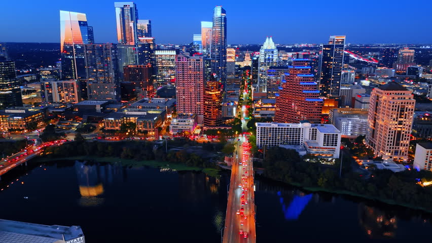 Numerous cars with headlights on move by the downtown. Flying over the bridge across the Colorado River at night. Austin, Texas, USA.