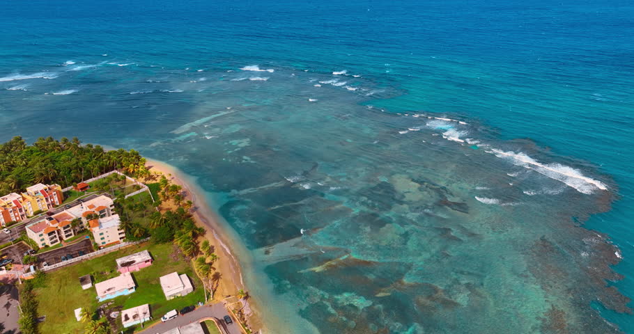 Splendid coast with clear turquoise water and waves rolling to the beach. Top view on the houses located in the palm trees. Puerto Rico.