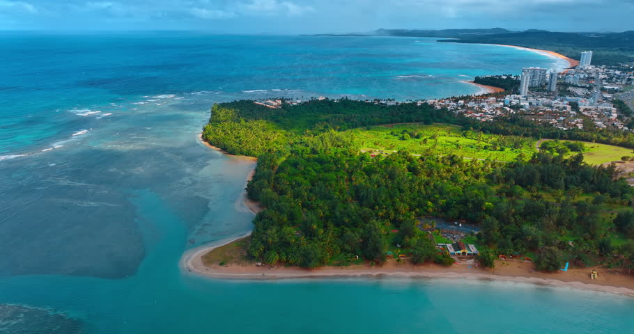 Beautiful coast covered with lush greenery. Turquoise water wash the land. Cityscape at the scenery at backdrop. Aerial view. Puerto Rico.