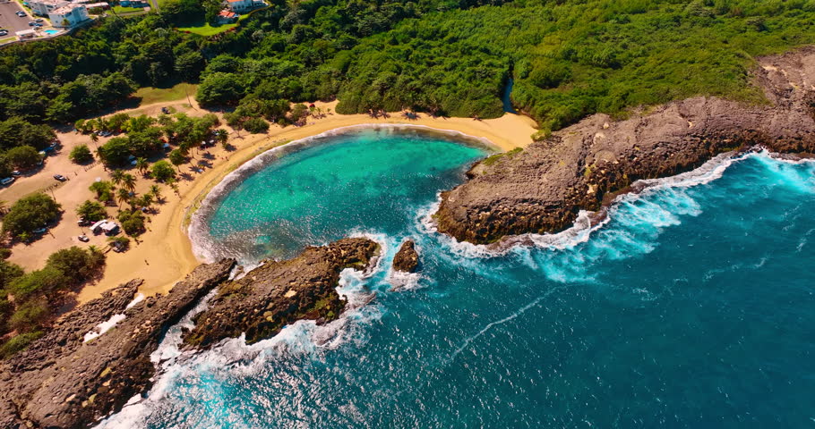Turquoise water of the Atlantic hitting the rocks that protect beautiful beach. Approaching Mar Chiquita Beach in Manati, Puerto Rico surrounded by lush greenery.