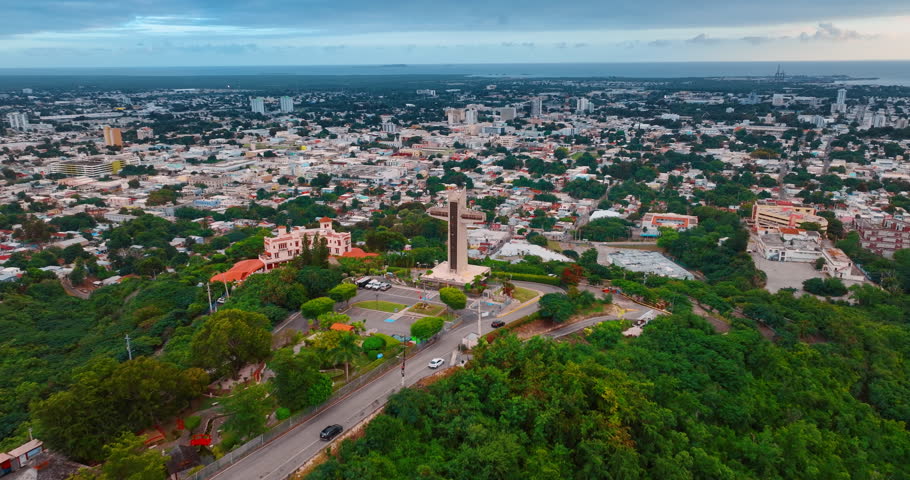 Distancing from a cross located on the hill covered with lush greenery. Vast cityscape on Ponce, Puerto Rico on a gloomy day.