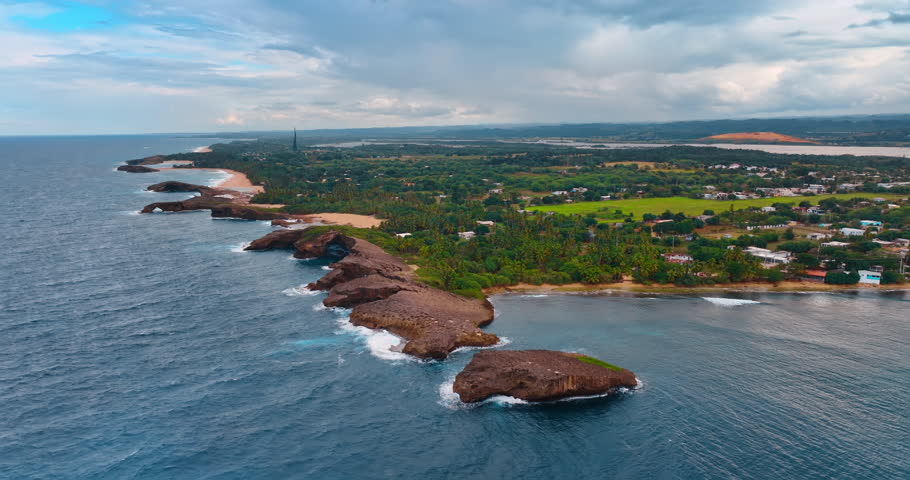 Flying to the rocks washed by the ocean waves at the coast. Multiple palm trees grow in the picturesque landscape. Puerto Rico.