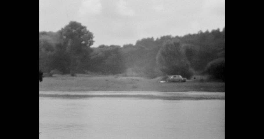 Natural landscape with trees and water, grainy texture. Vintage black and white footage of a scenic forest lake and distant shoreline.