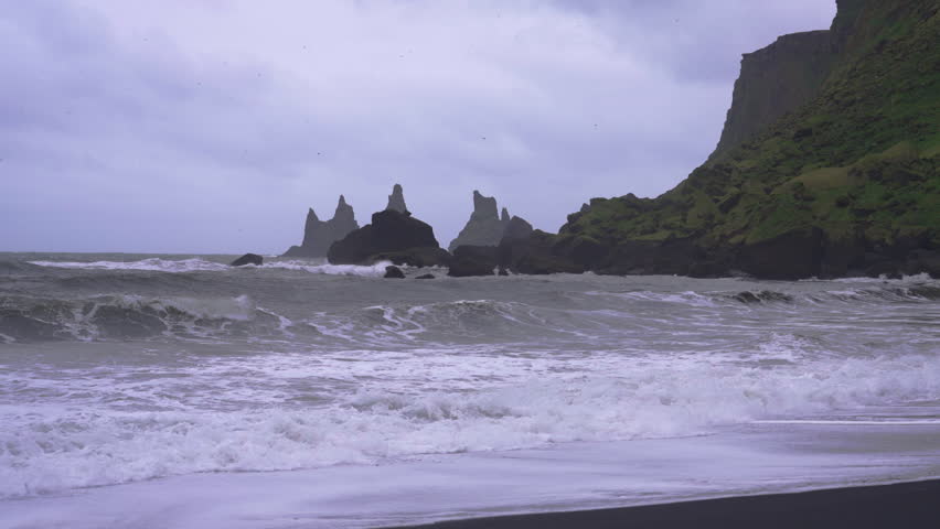 Waves crashing on black sand beach near mountains in Vik, Iceland