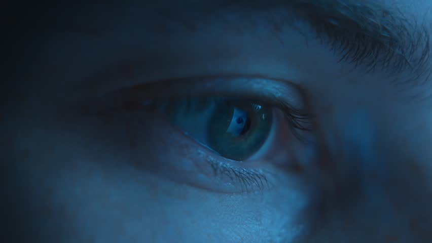 Close-up of a human eye intently looking at a glowing screen illuminated by blue light, while viewing social media feeds or working late at night. 