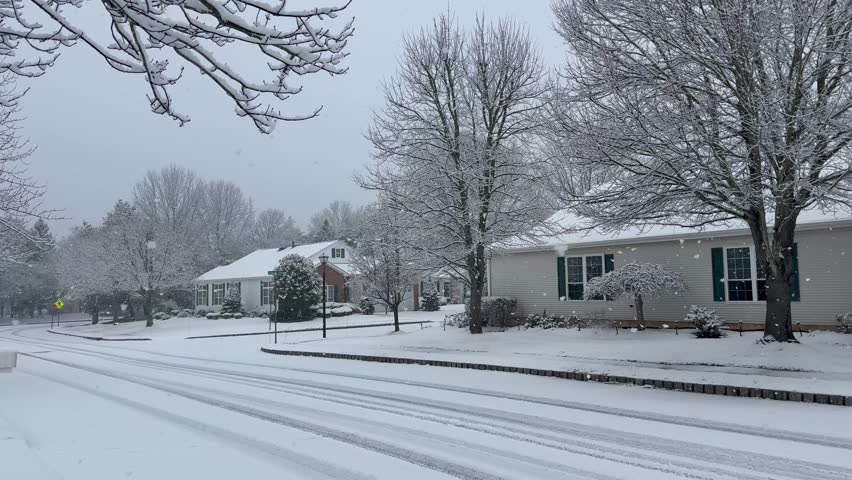 Quiet neighborhood with snow falling on snow covered streets and houses