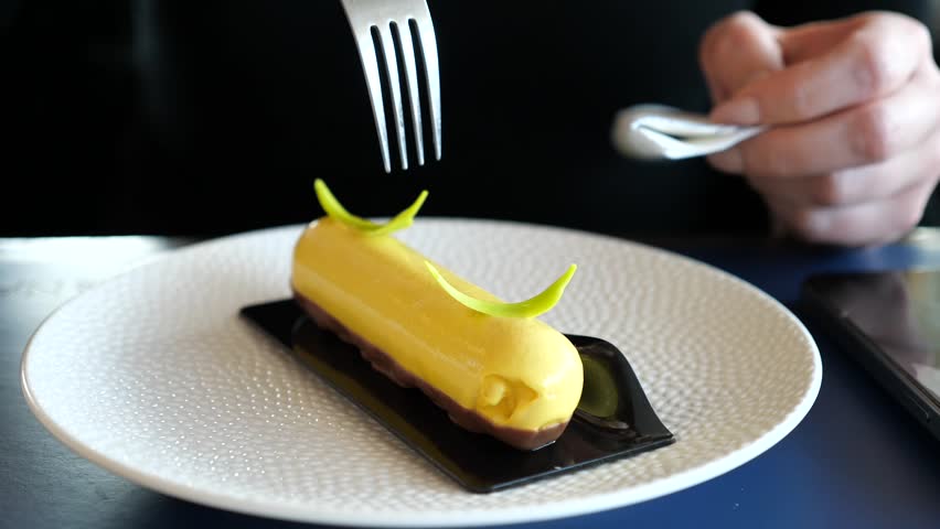 Elegant yellow yuzu lemon petit gateau dessert on white plate, eaten with a fork at a restaurant. 
