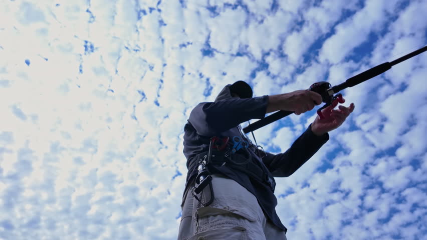 View up from below of an angler cast and reel casting rod and using walk the dog technique fishing action with top water lure to catch top water fish such as smallmouth or largemouth bass.