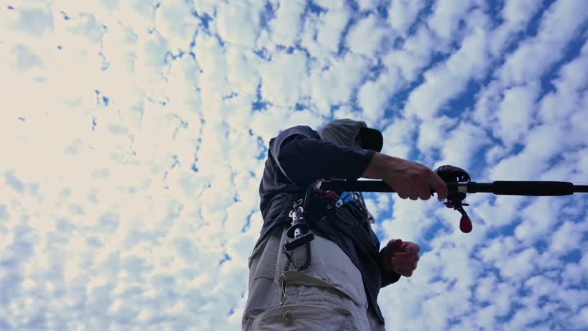 View up from below of an angler cast and reel casting rod and using walk the dog technique fishing action with top water lure to catch top water fish such as smallmouth or largemouth bass.