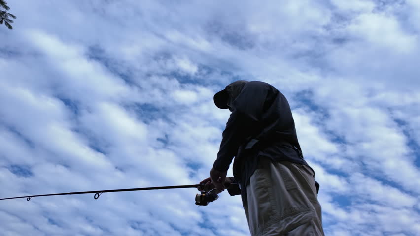 Man fishing at serene lake from the boat dock, casting fishing spinning rod and using reel. Sport angler during fishing summer vacation.