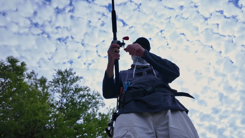 View up from below of an angler cast and reel casting rod and using walk the dog technique fishing action with top water lure to catch top water fish such as smallmouth or largemouth bass.