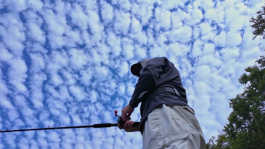 View up from below of an angler cast and reel casting rod and using walk the dog technique fishing action with top water lure to catch top water fish such as smallmouth or largemouth bass.