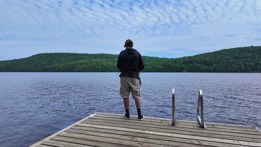 Man fishing at serene lake from the boat dock, casting fishing spinning rod and using reel. Sport angler during fishing summer vacation.
