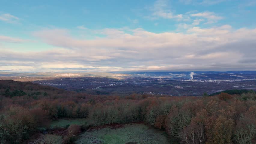 Drone flying over a beautiful view of a city with a large mountain in the background. The sky is clear and the sun is shining in Orense, Spain.