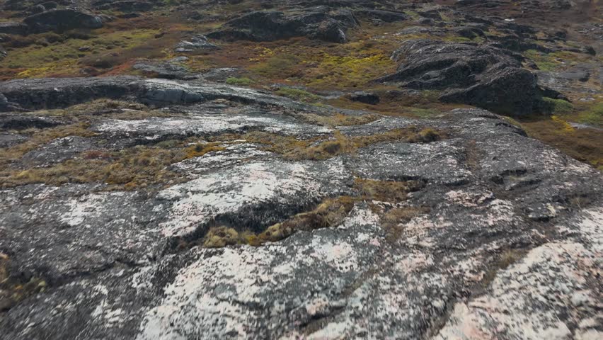 Rocky Greenland coastline reveals abandoned fishing village and distant sailing boat