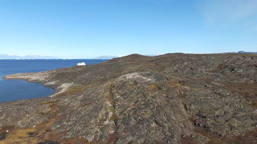 Near Greenland coast, rugged rocks lead toward iceberg and open sea