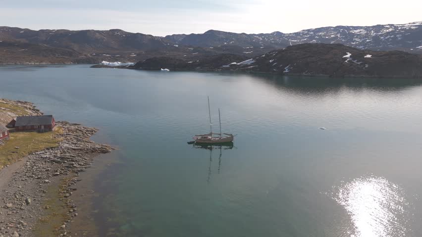 Large sailing boat anchors near abandoned Greenland fishing village coastline