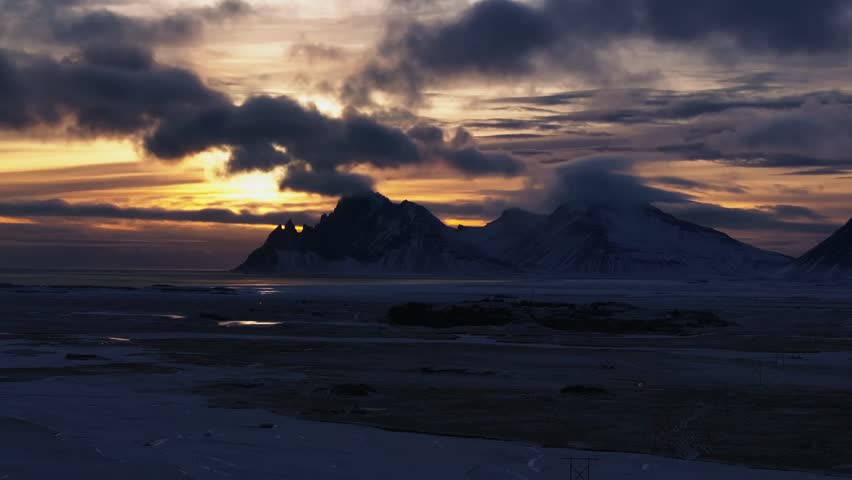Dramatic glowing sunset beyond Vestrarhorn landmark, Iceland winter landscape - aerial 4k