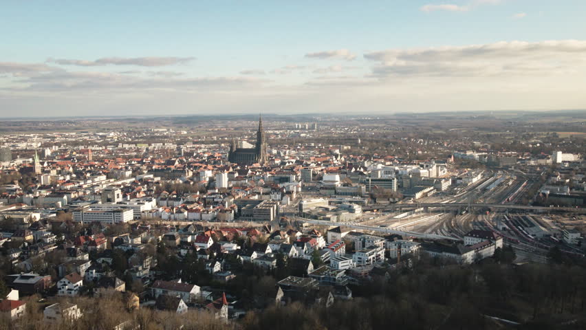 4K aerial drone descending through forest canopy toward Ulm cityscape and cathedral. Premium footage capturing woodland, city landmarks, and panoramic landscape. Perfect for nature and travel document