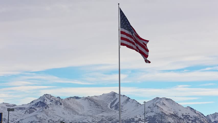 American flag proudly waving against the backdrop of snow-covered mountaines in Anchorage. American state Alaska.