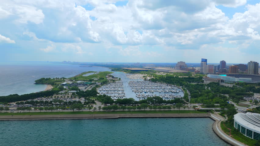 Wide aerial panorama of Chicago Illinois harbor and Lake Michigan showing curved shoreline, marina docks, open water, distant skyline, cloudy sky, and coastal city scale
