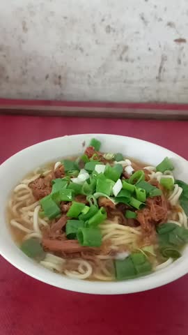 A bowl of warm chicken noodle soup topped with shredded chicken and spring onions.