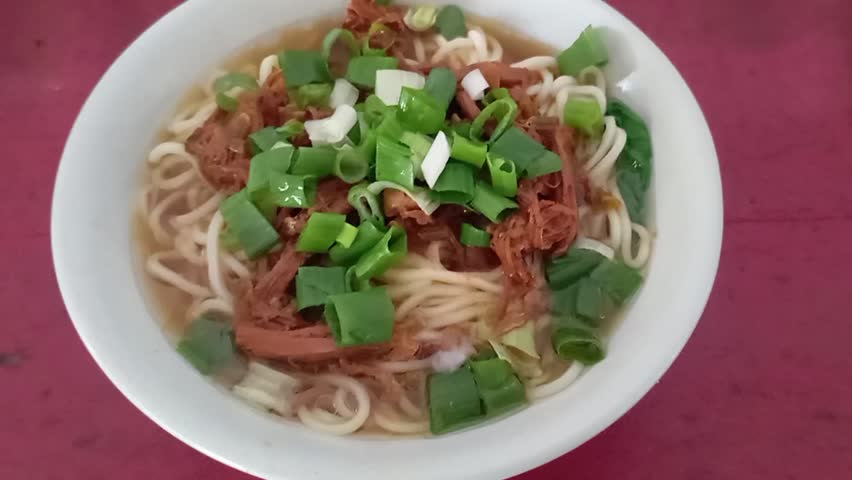 A bowl of warm chicken noodle soup topped with shredded chicken and spring onions.